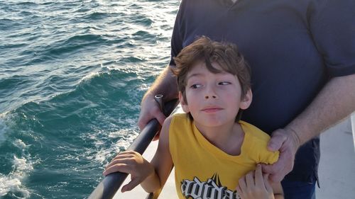 Son looking away while standing with father on sailboat