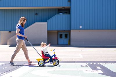 Side view of woman pushing her daughter sitting on tricycle during sunny day