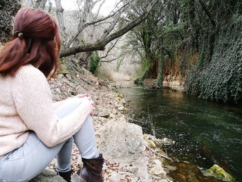 Side view of woman sitting by lake at park