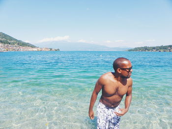 Portrait of shirtless man standing in sea against sky