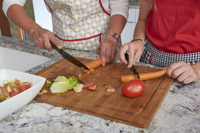 Midsection of mother and daughter preparing salad in kitchen at home