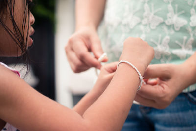 Close-up of mother and daughter repairing pearl necklace