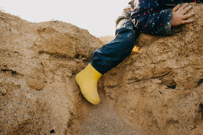 Child with yellow rubber boots playing on sand