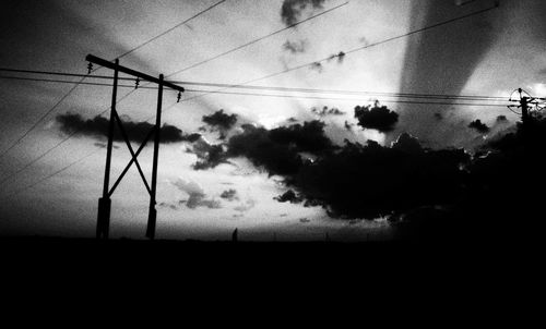 Low angle view of electricity pylon against cloudy sky