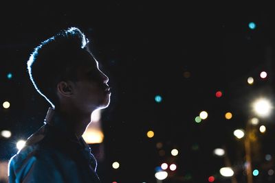 Close-up of boy standing against illuminated sky at night