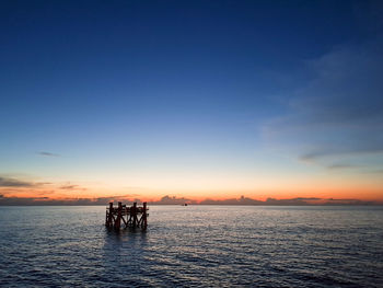 Silhouette people at sea against sky during sunset