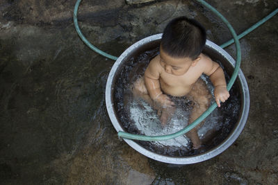 High angle view of shirtless baby boy sitting in water filled container