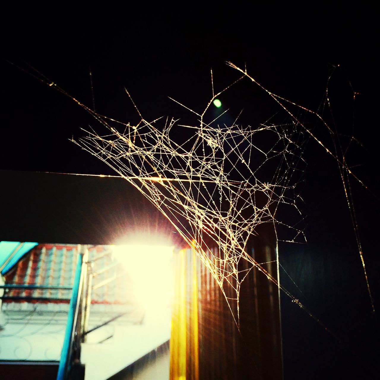 night, illuminated, low angle view, built structure, architecture, lighting equipment, building exterior, long exposure, outdoors, sky, spider web, electricity, no people, connection, glowing, light - natural phenomenon, fence, motion, light, branch