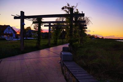 Footpath by building against sky at sunset