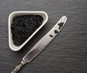 Grainy caviar of paddlefish fish in a white ceramic plate and a knife near, black backgroun