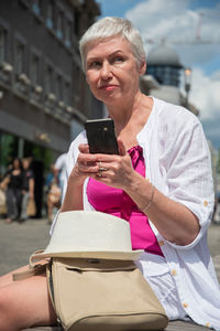 Grey haired aged caucasian woman in summer clothes chats in mobile in the city