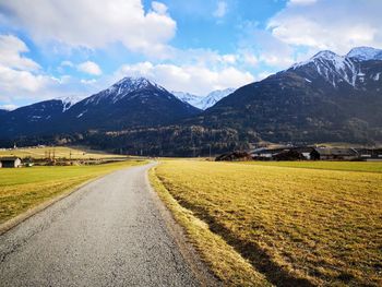 Road amidst field and mountains against sky
