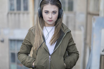 Close-up portrait of young woman listening music with hands in pocket