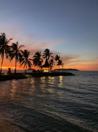 Silhouette palm trees by the seashore against sky during sunset