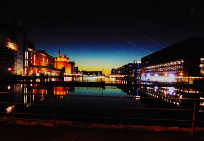 Illuminated buildings by river against sky at night