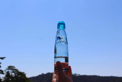 Close-up of hand holding bottle against blue sky