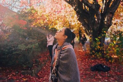 Side view of young woman standing by tree during autumn