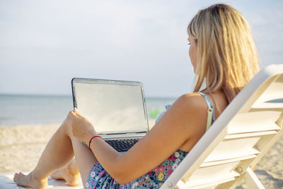 Young woman using laptop while sitting at beach