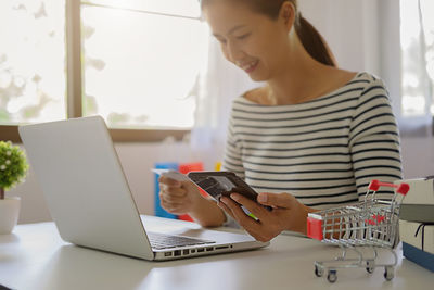 Businesswoman holding credit card while using laptop on table