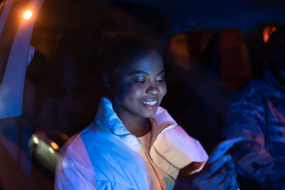 Smiling afro american woman sitting in car on passenger seat with smartphone, using social media app