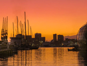 Sailboats in harbor against orange sky