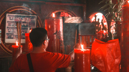 Rear view of man with illuminated candles in temple