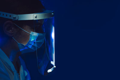 Close-up of doctor wearing face shield against blue background