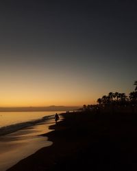 Silhouette person on beach against clear sky during sunset