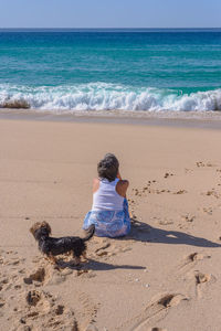 Dog behind woman sitting on sandy beach