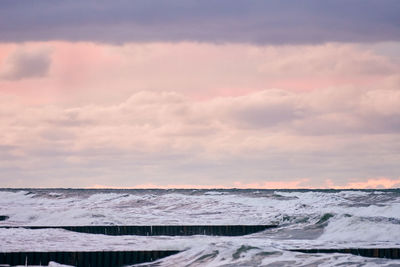 Scenic view of purple cloudy sky and sea with foaming waves. vintage long wooden breakwaters in sea