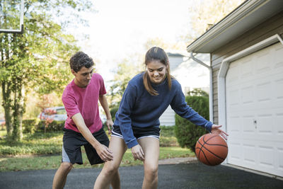 Happy brother and sister playing basketball at backyard