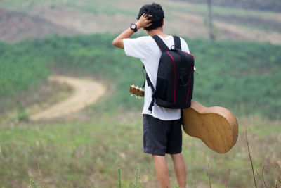 Rear view of man standing with guitar on field