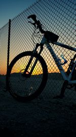Bicycle on chainlink fence against sky