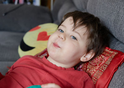 Expressive young boy eating an apple and lounging on the couch at home