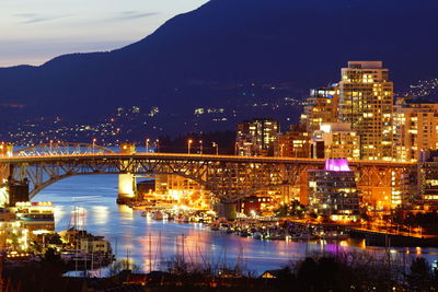 Illuminated bridge over river amidst buildings in city at night