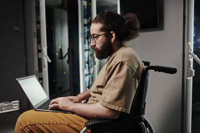 It expert sitting on wheelchair using laptop in server room