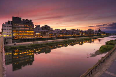 Reflection of buildings in river against sky during sunset