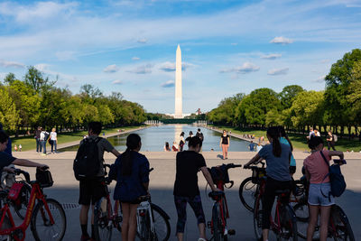 Rear view of people on bicycle by trees against sky