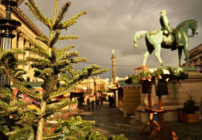 Sculpture of people by plants against sky