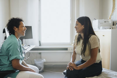 Smiling mature doctor and female patient discussing while sitting in clinic