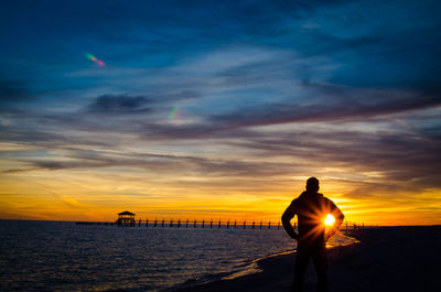 Silhouette man standing at beach against dramatic sky during sunset