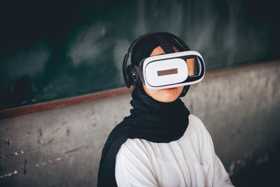 High angle view of young woman looking through virtual reality simulator while sitting against wall