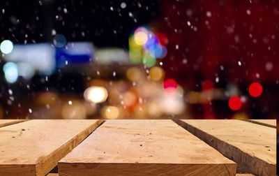 Close-up of wooden walkway against colorful lights in city during winter