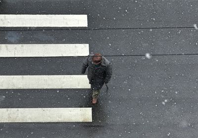 High angle view of man crossing road in city during snowfall