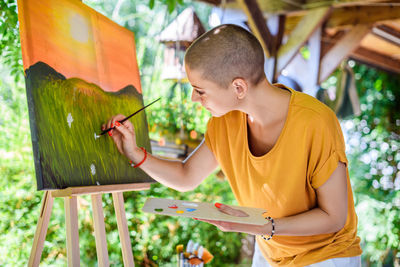 Young female artist working on her art canvas painting outdoors in her garden. 