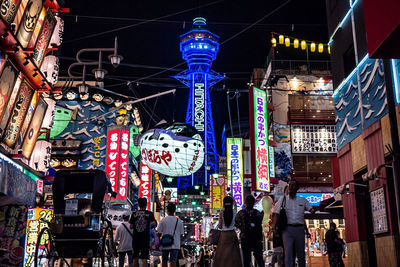 People on illuminated street amidst buildings in city at night