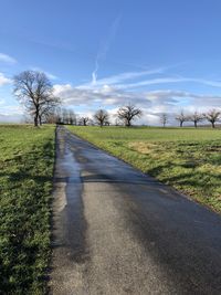 Empty road amidst field against sky