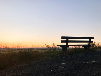 Empty bench on field against clear sky during sunset