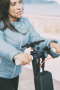 Beautiful middle-aged woman in blue jacket rides electric scooter