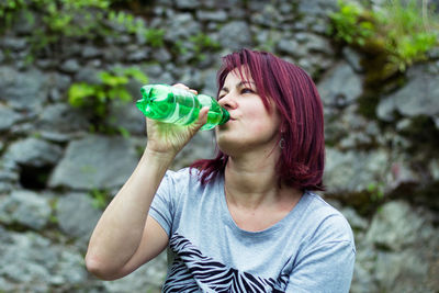 Woman drinking water from bottle against stone wall